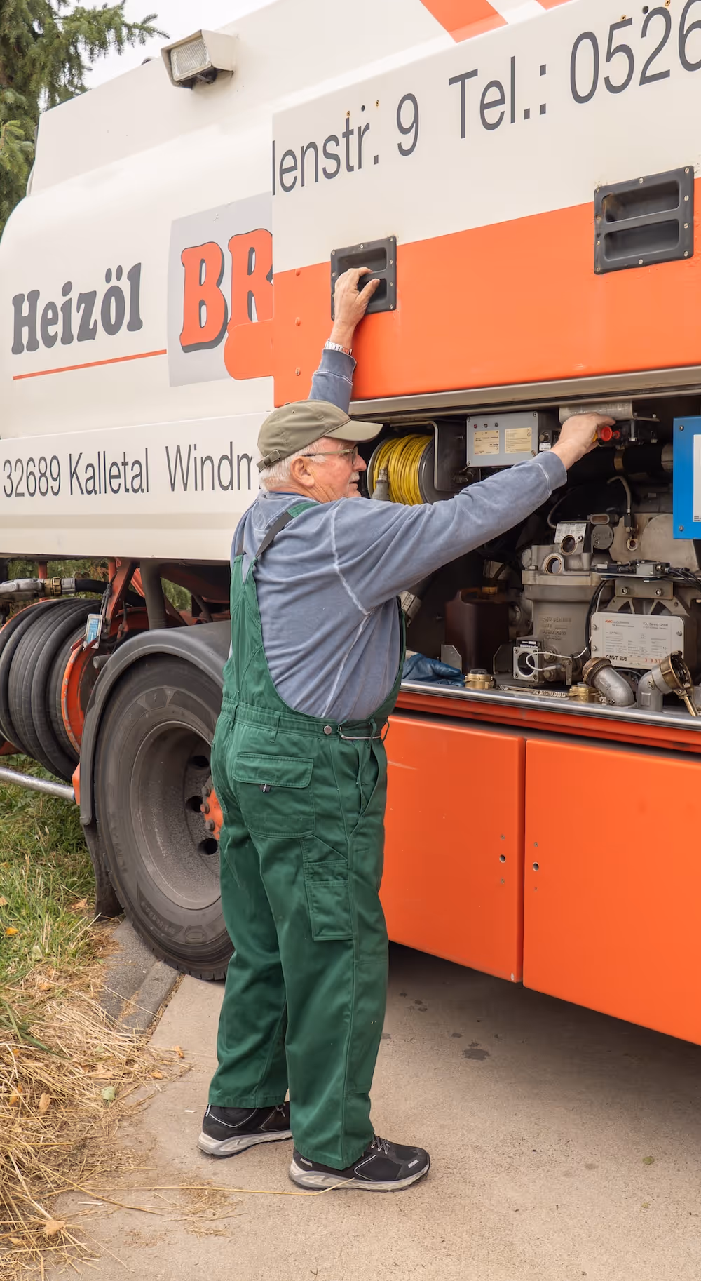 Älterer Mann in grüner Arbeitskleidung repariert einen Heizöllieferwagen.
