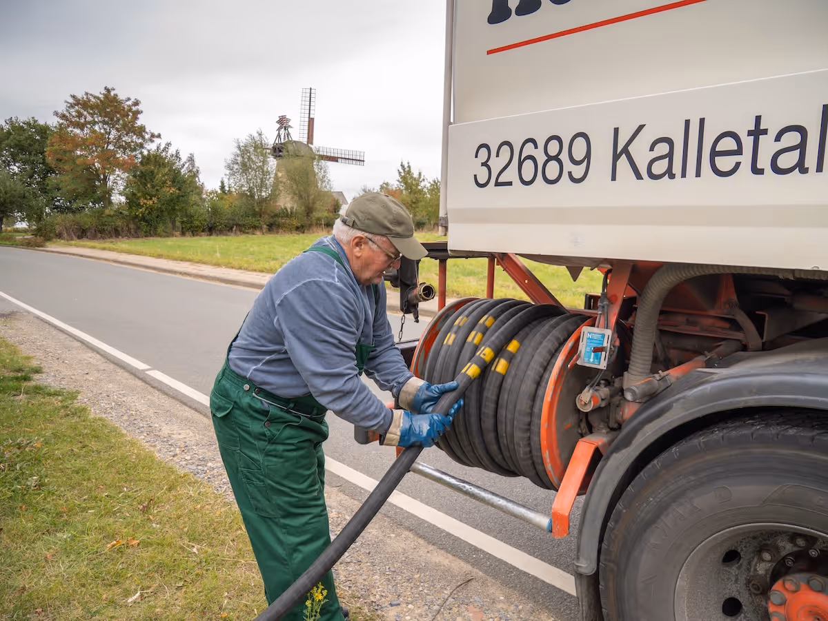 Älterer Mann mit blauen Handschuhen rollt Schlauch an einem Fahrzeug neben einer Landstraße ab.