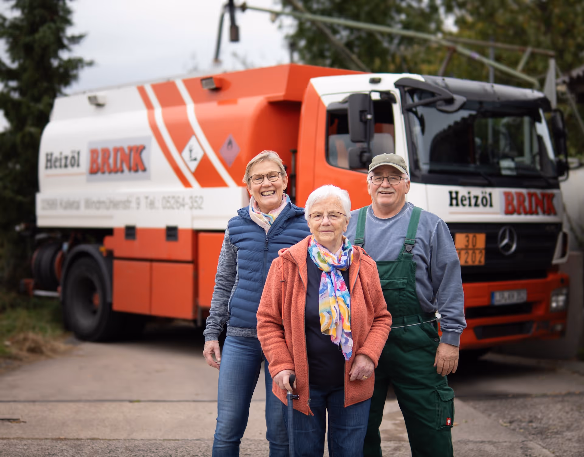 Drei ältere Menschen vor einem roten Heizöl-Brink-Lieferwagen, zwei Frauen und ein Mann lächeln.