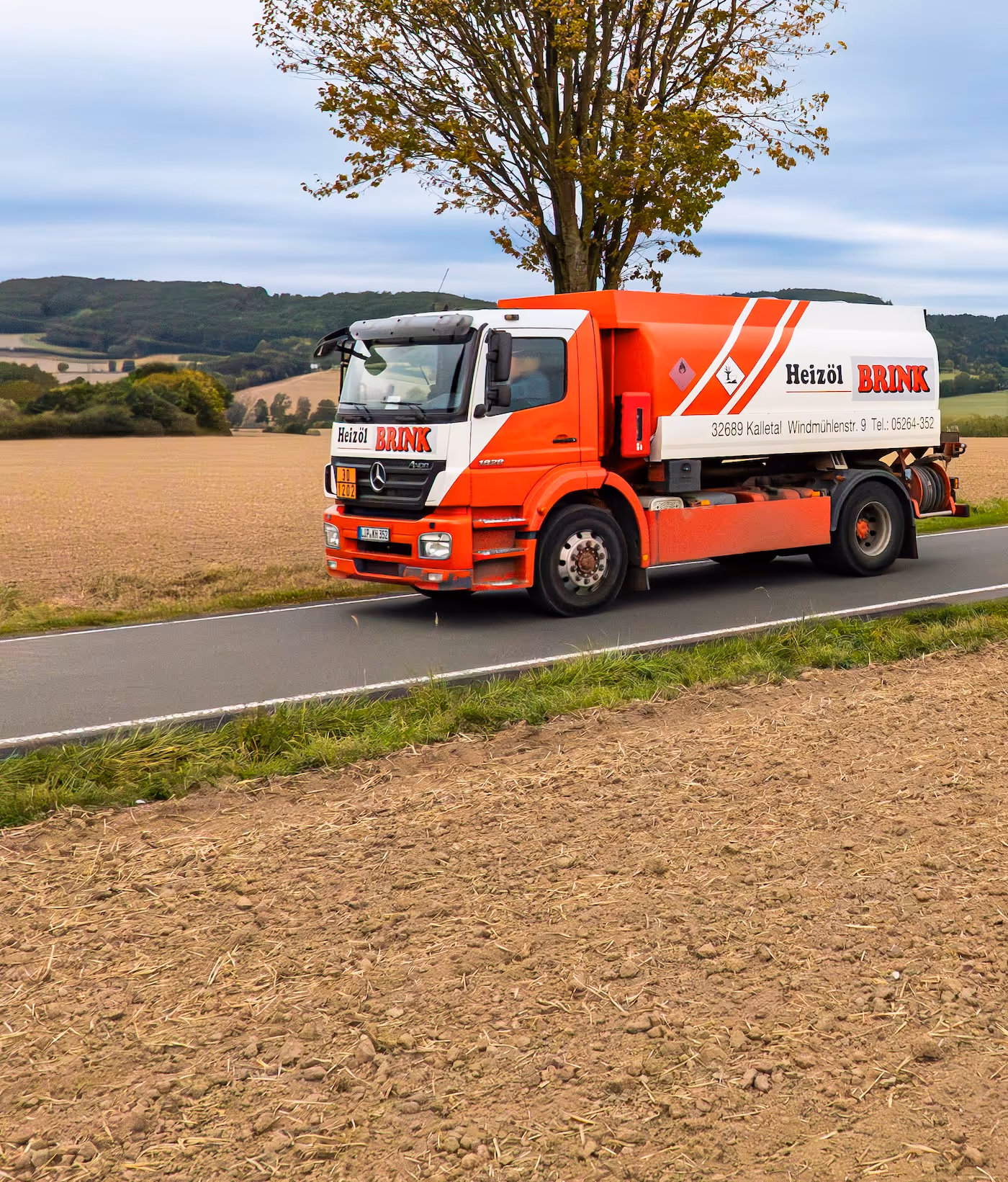 Roter Heizöl-LKW der Marke Brink fährt auf Landstraße neben Feldern und Baum.